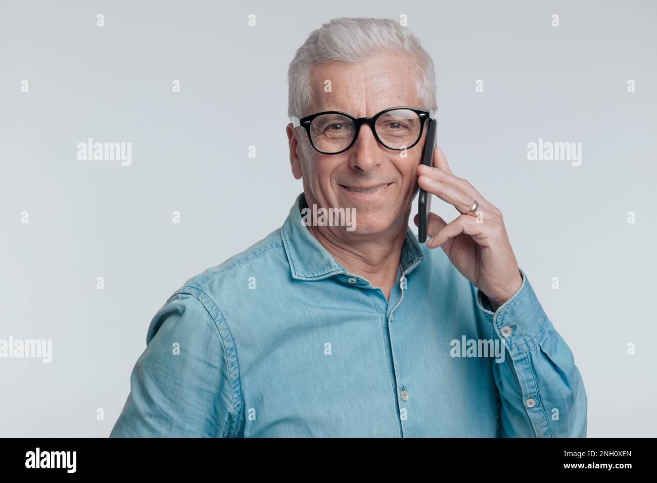 Porträt eines Gelegenheitsmannes in seinen 60s, der am Telefon spricht und auf grauem Hintergrund lächelt Stockfoto