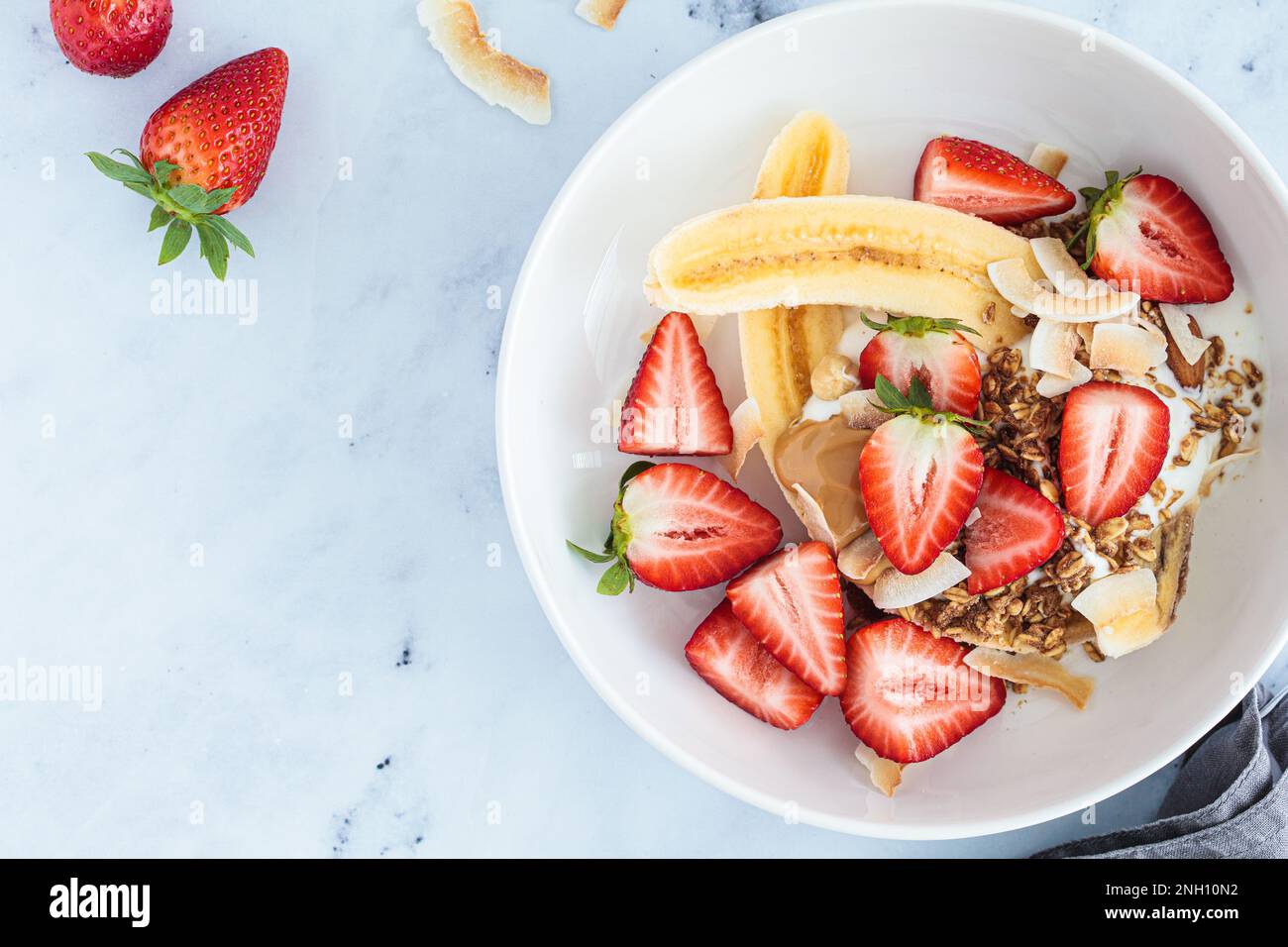 Gesundes veganes Bananensplit-Rezept mit griechischem Joghurt, Erdbeeren, hausgemachtem Müsli und Bio-Erdnussbutter, Draufsicht, Kopierbereich. Stockfoto
