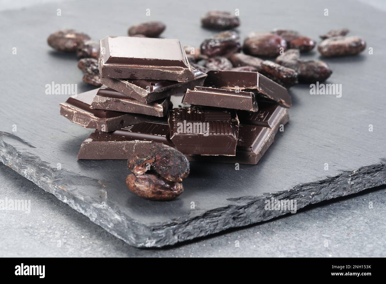 Zerbrochene dunkle Schokolade und Kakaobohnen auf einem Tisch Stockfoto