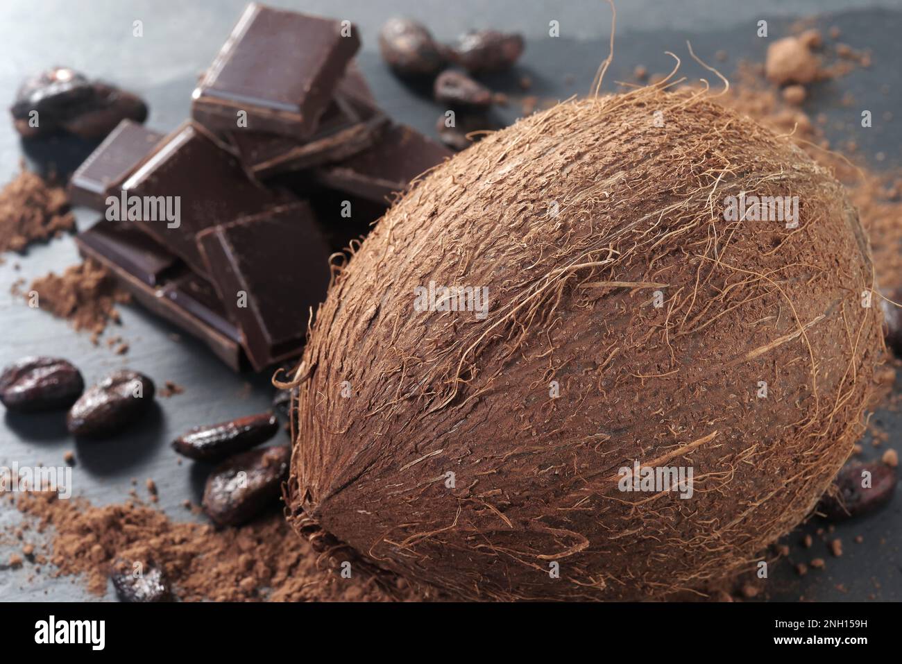 Zerbrochene dunkle Schokolade, Kakaobohnen und Kokosnuss auf dem Tisch Stockfoto
