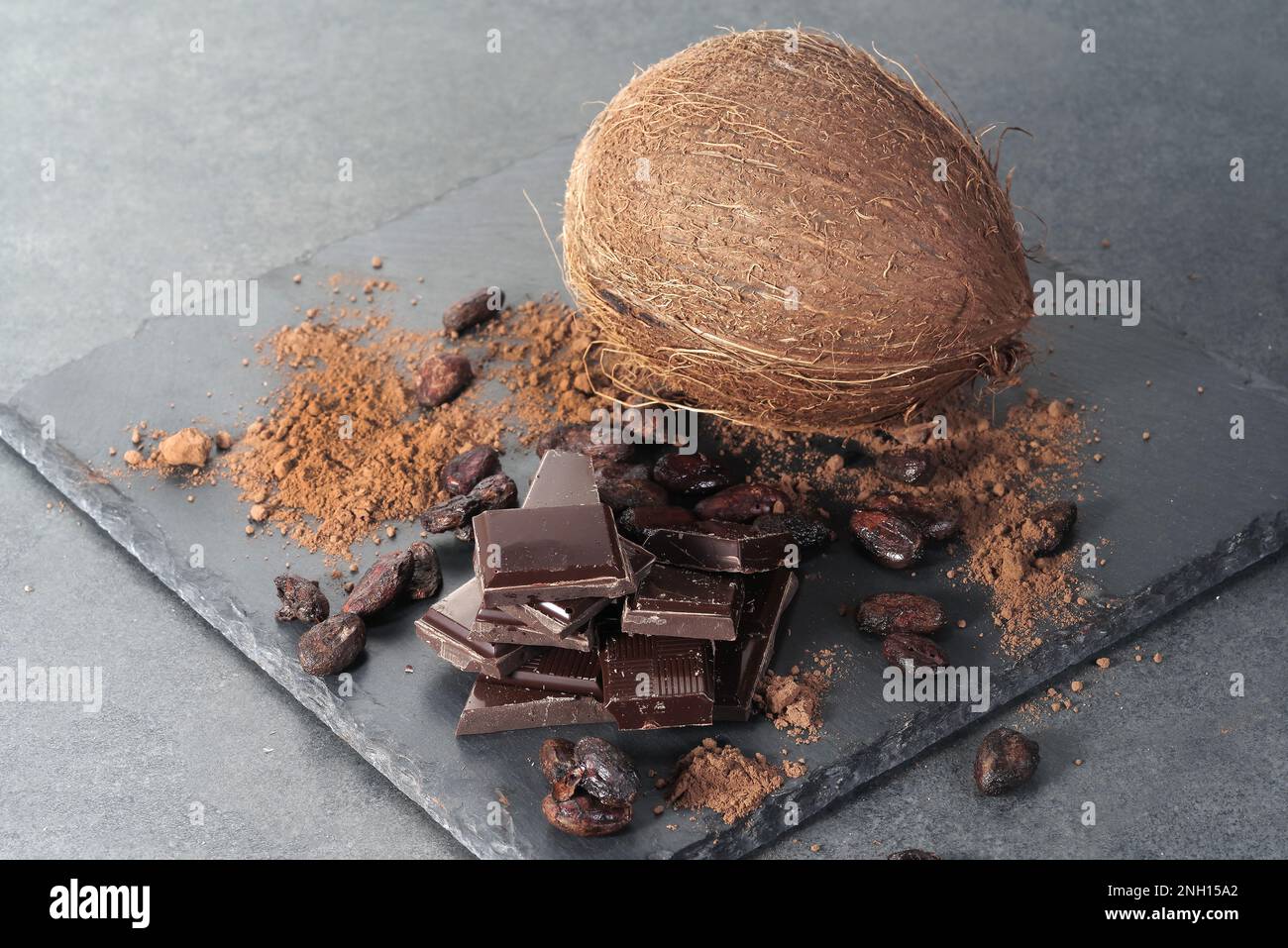 Zerbrochene dunkle Schokolade, Kakaobohnen und Kokosnuss auf dem Tisch Stockfoto