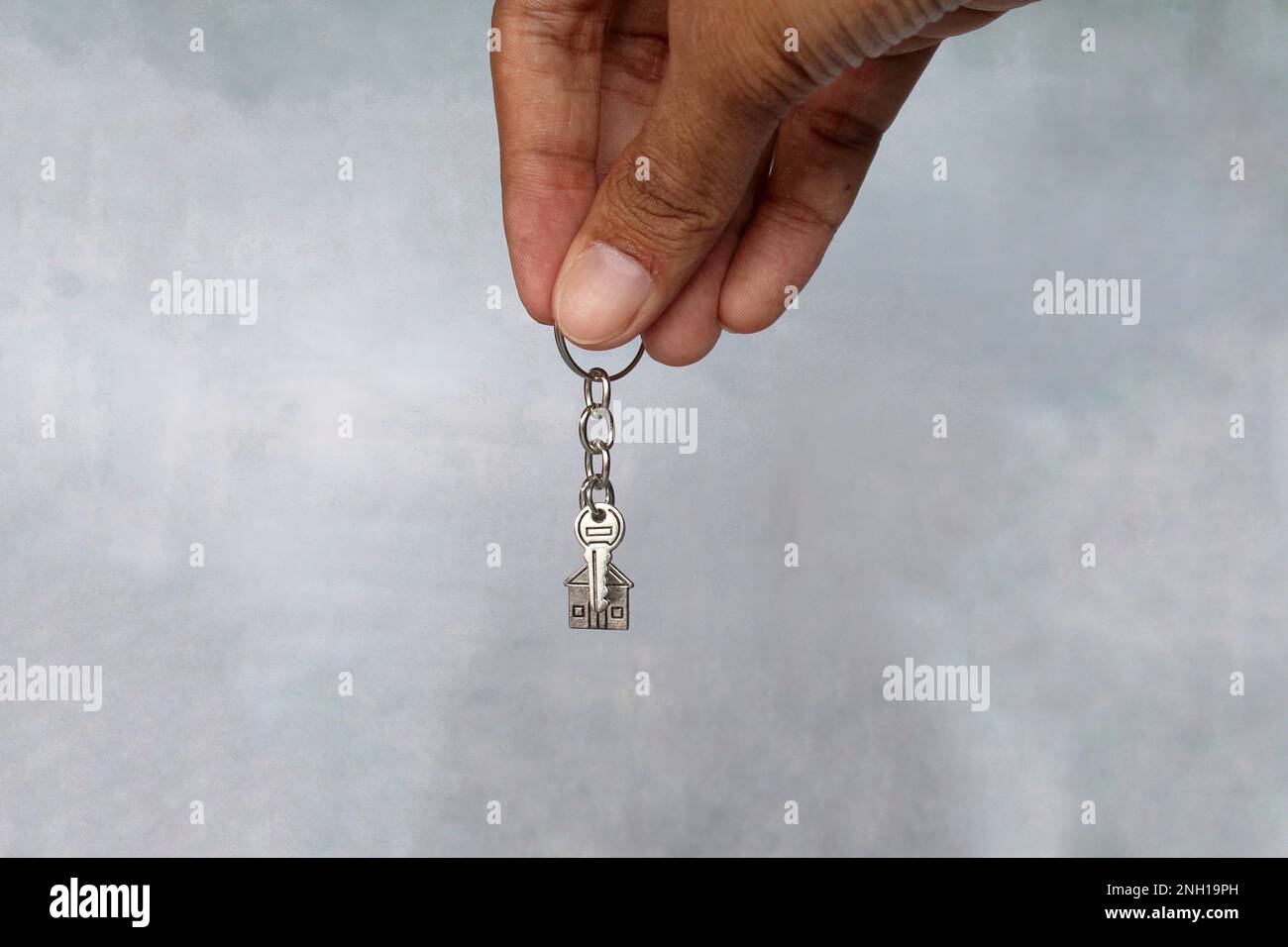 Handgehaltener Schlüsselanhänger in Hausform und Schlüssel mit Kopierbereich. Hausbesitzkonzept. Stockfoto