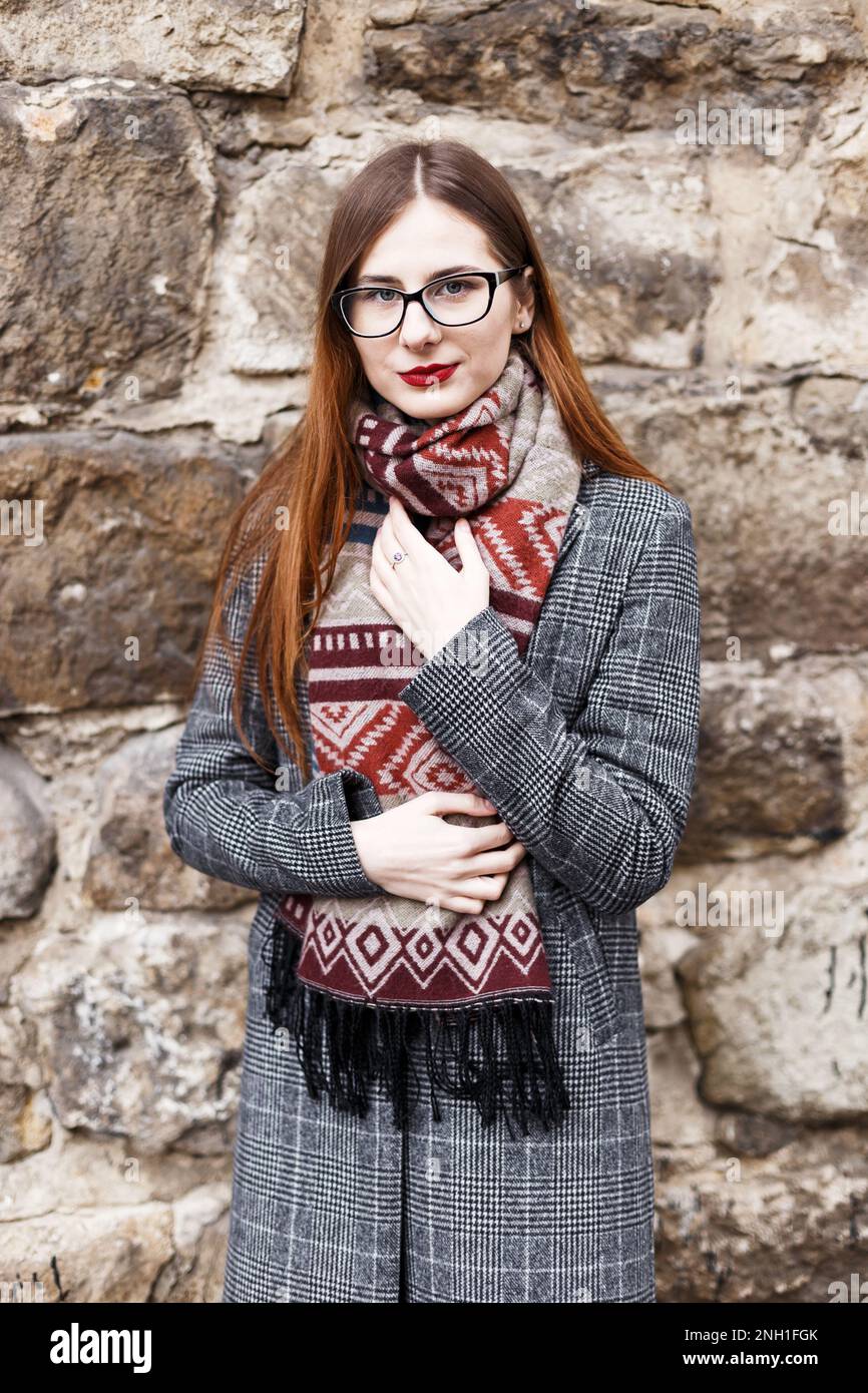Junge Frau in Brille, die einen Mantel in einem Schal trägt Stockfoto