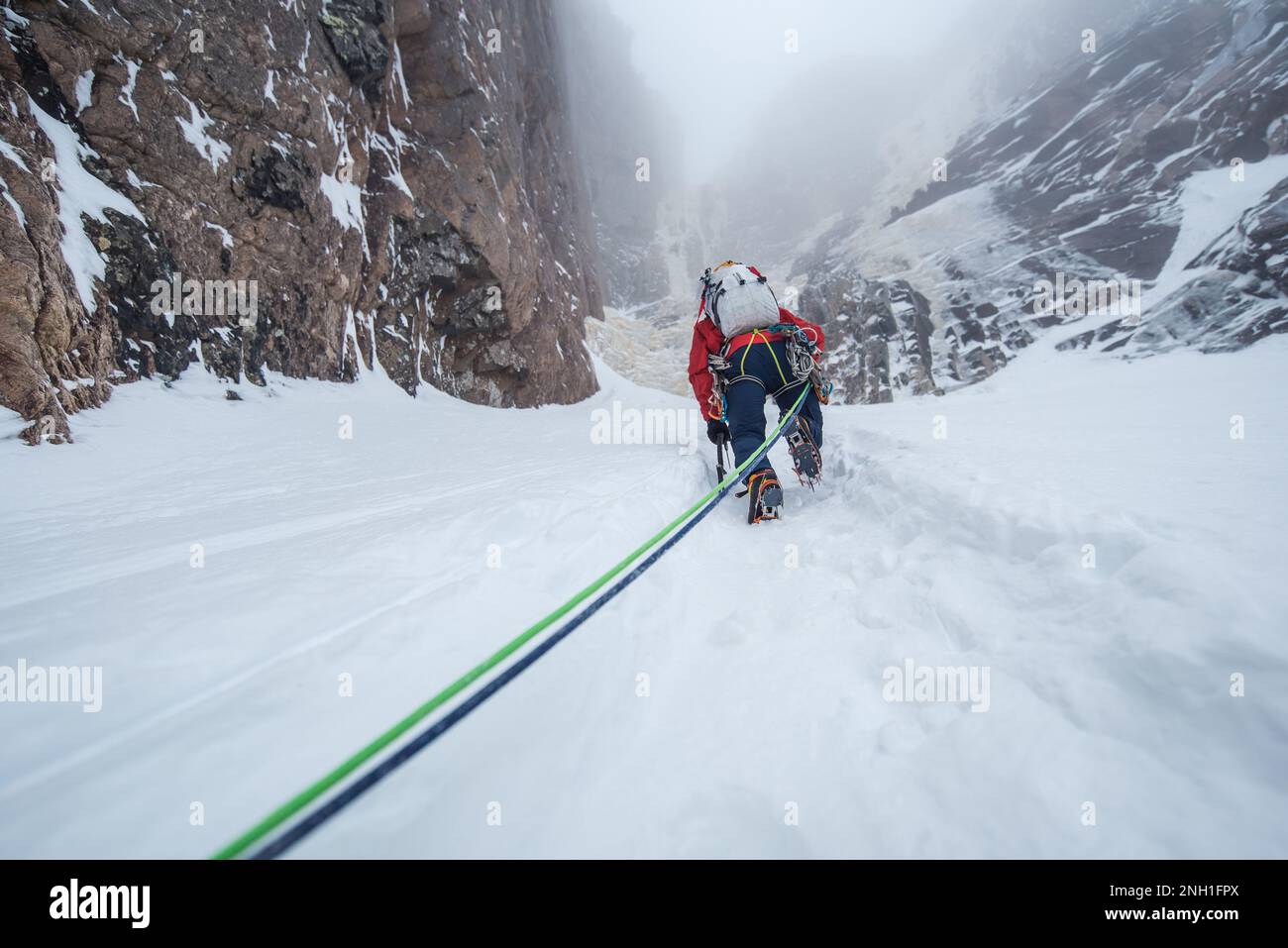 Eiskletterer klettert Schnee, um an die Felswand zu gelangen Stockfoto