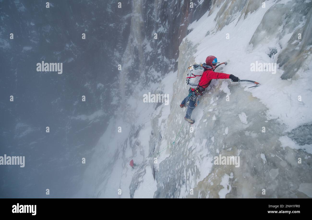 Eiskletterer klettert steile Eismauer mit Felsen um ihn herum Stockfoto