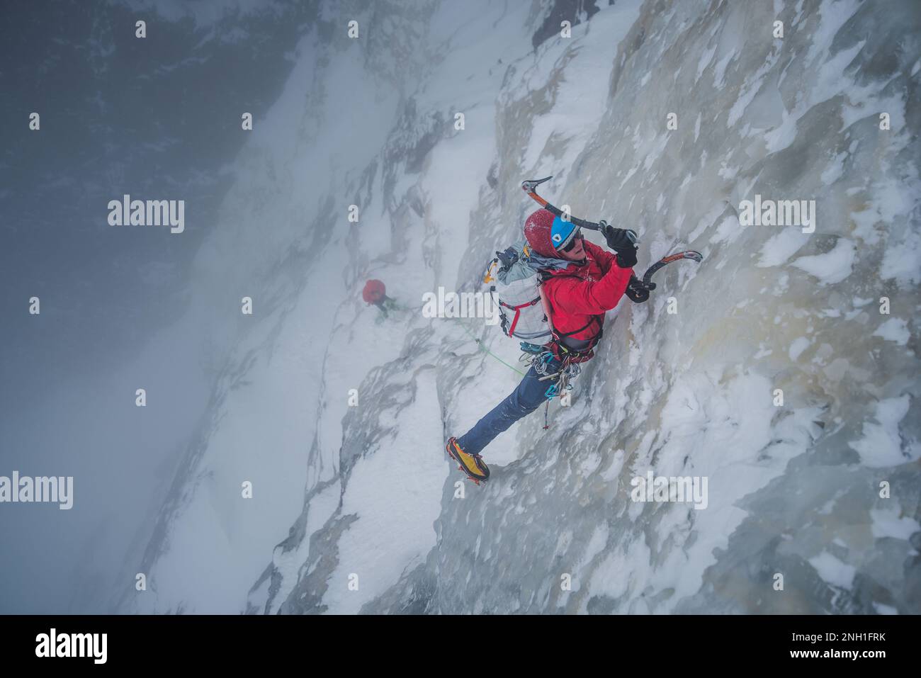 Eiskletterer klettert steile Eismauer mit Felsen um ihn herum Stockfoto