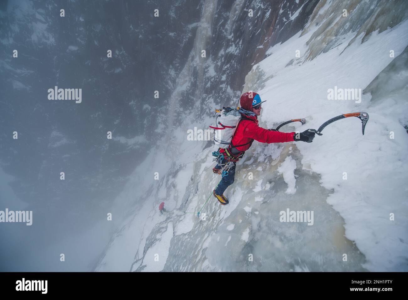 Eiskletterer klettert steile Eismauer mit Felsen um ihn herum Stockfoto