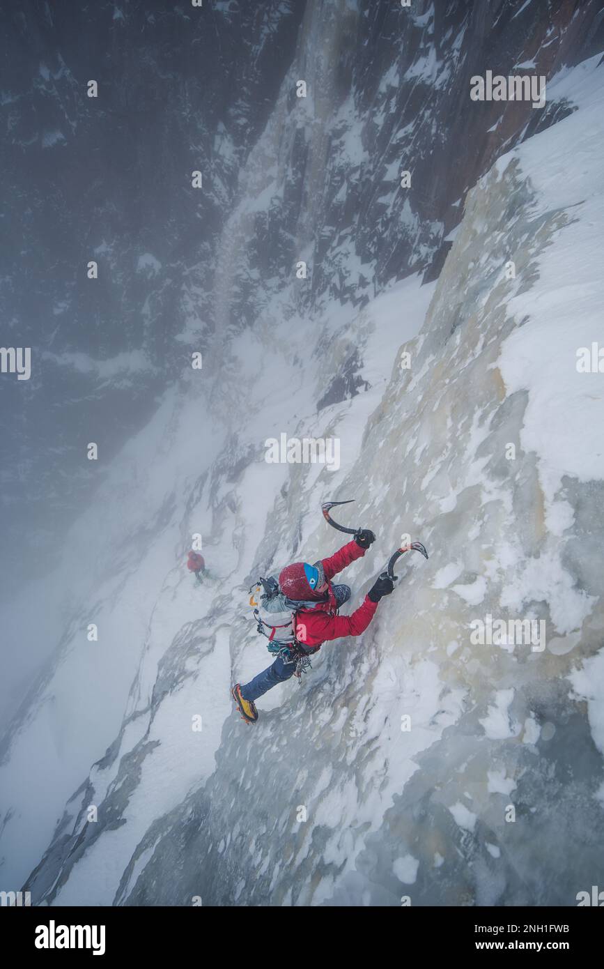 Eiskletterer klettert steile Eismauer mit Felsen um ihn herum Stockfoto