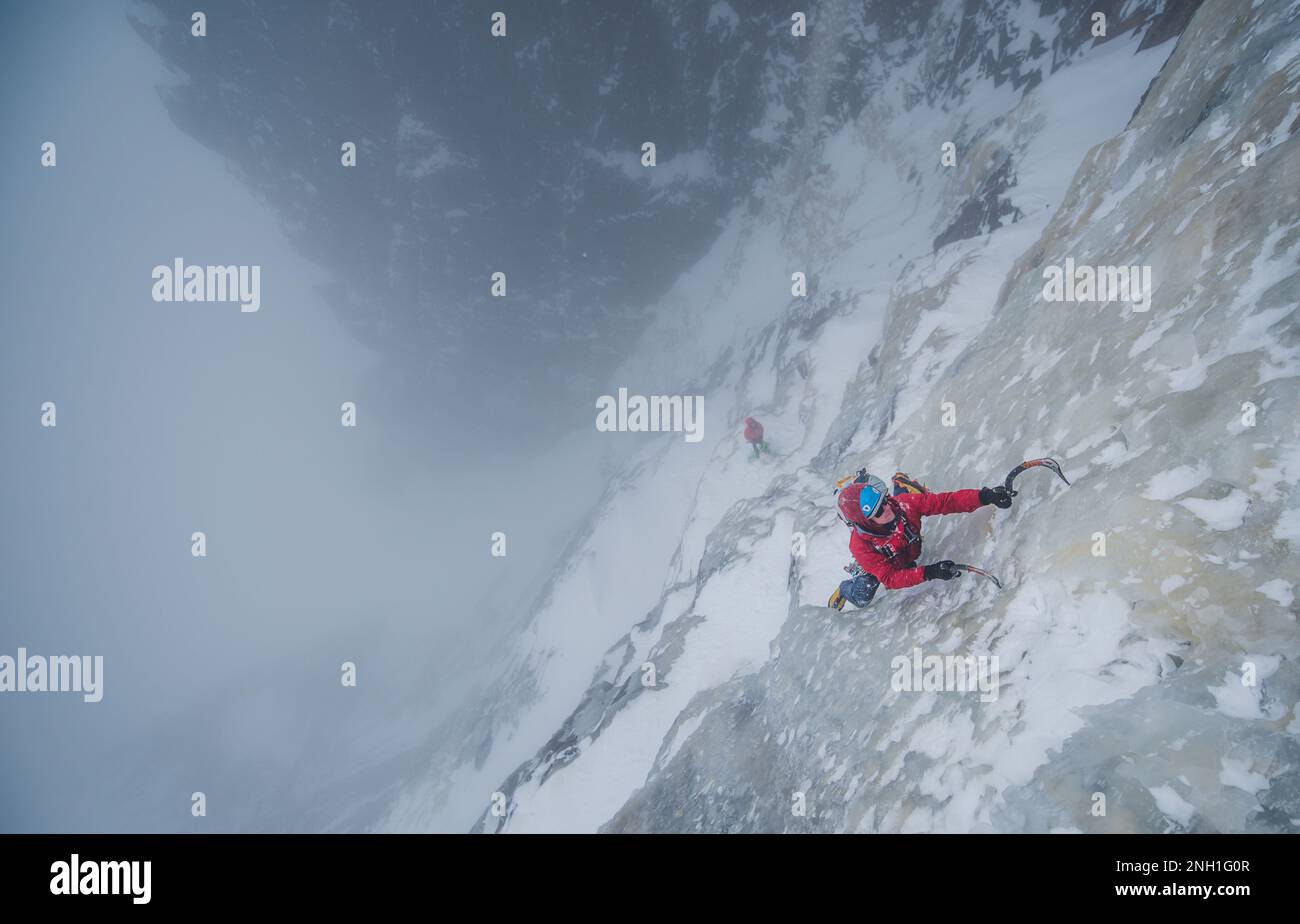 Eiskletterer klettert steile Eismauer mit Felsen um ihn herum Stockfoto