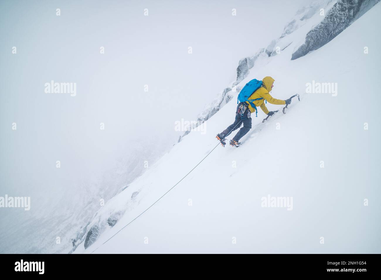 Männlicher Bergsteiger klettert bei kalten Temperaturen auf steile Schneefelder Stockfoto