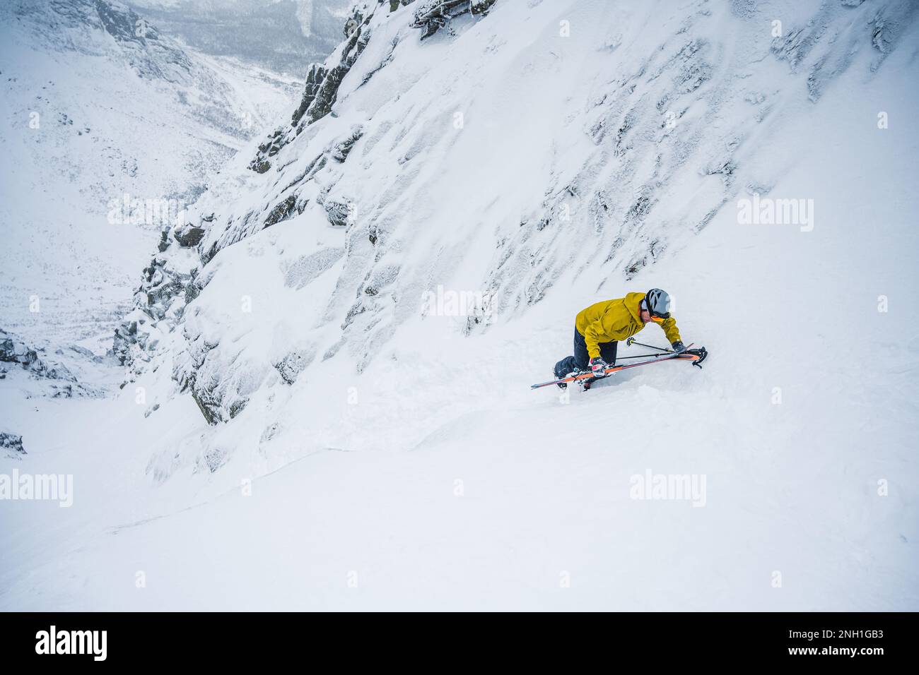 Skifahrer in gelber Jacke klettert zurück auf die Spitze der Skipiste Stockfoto