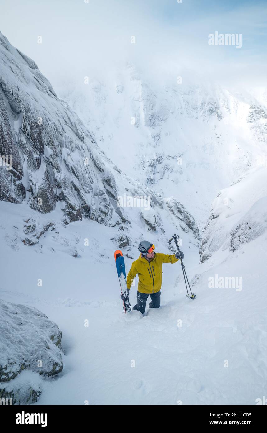 Skifahrer in gelber Jacke klettert zurück auf die Spitze der Skipiste Stockfoto