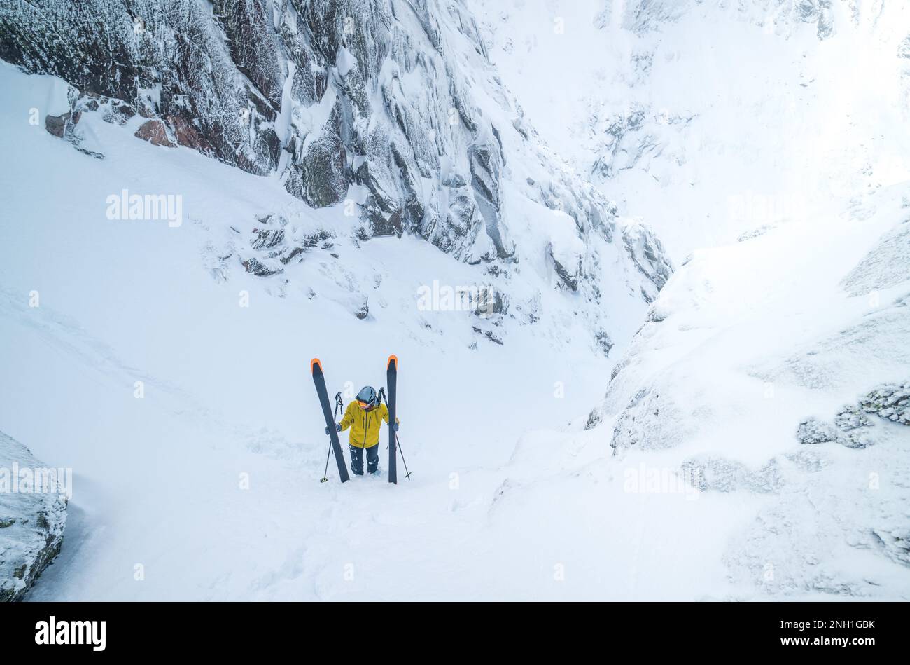 Skifahrer in gelber Jacke klettert zurück auf die Spitze der Skipiste Stockfoto