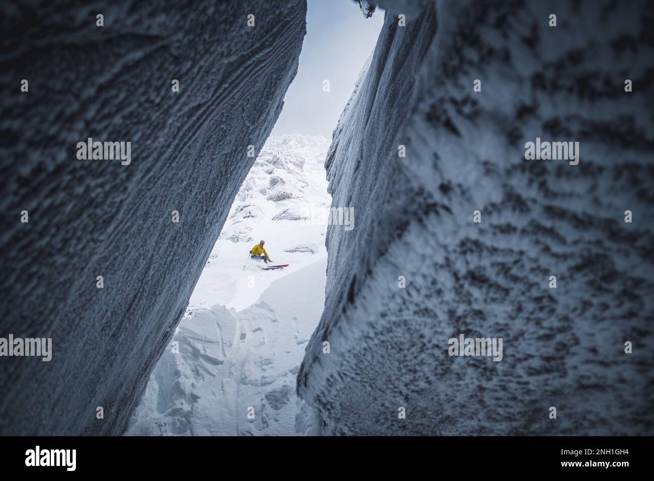 Skifahrer in einer gelben Jacke, der Schnee in eine Eishöhle hinabgleitet Stockfoto