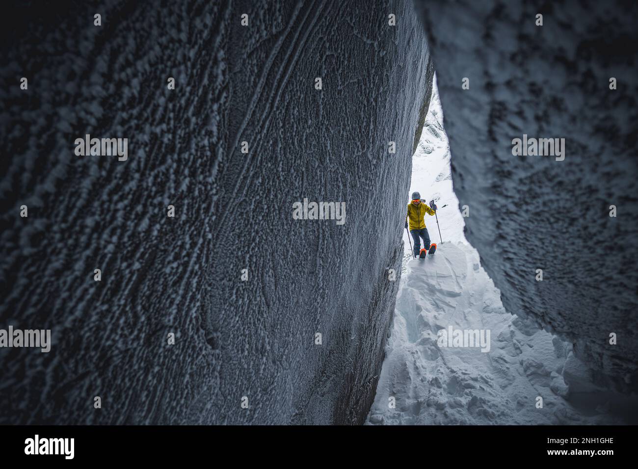 Skifahrer in einer gelben Jacke, der Schnee in eine Eishöhle hinabgleitet Stockfoto