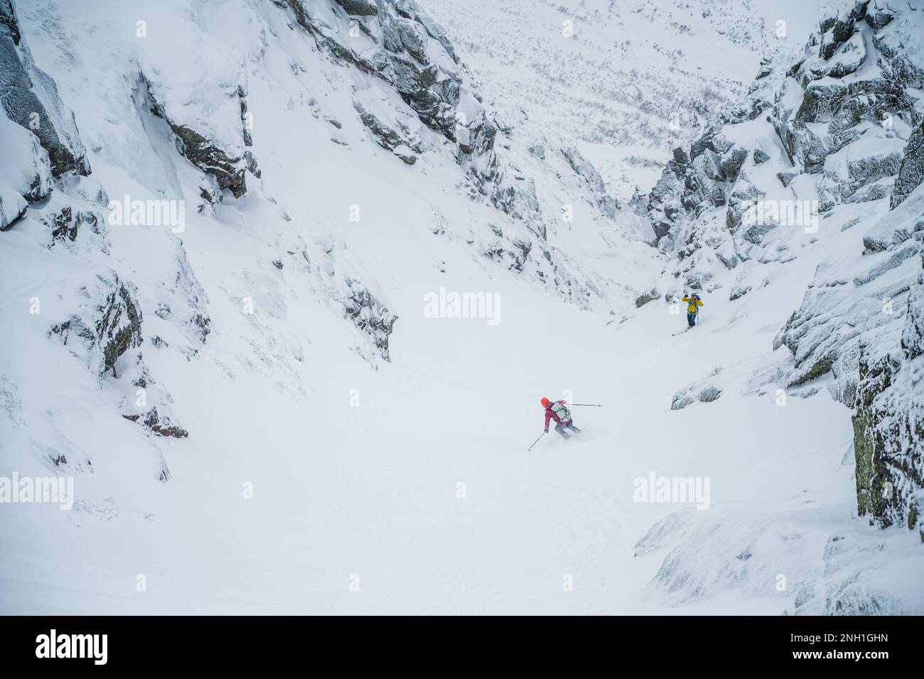 Skifahrer, die in einer Schlucht mit umliegenden Felswänden fahren Stockfoto