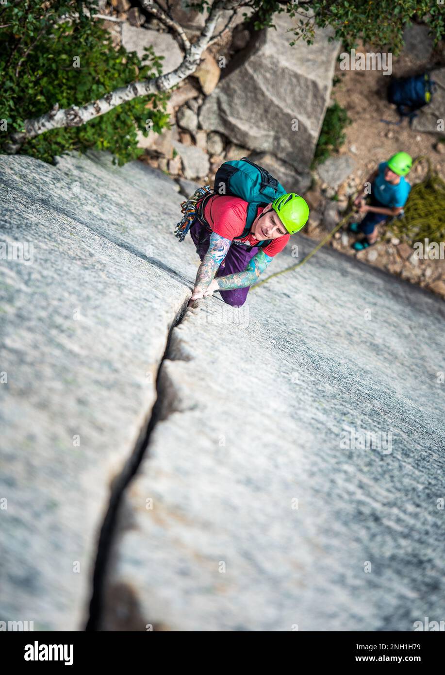 Ein Mann mit Tattoos klettert einen Riss an einer Felswand Stockfoto