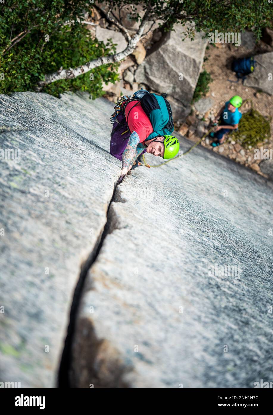Ein Mann mit Tattoos klettert einen Riss an einer Felswand Stockfoto