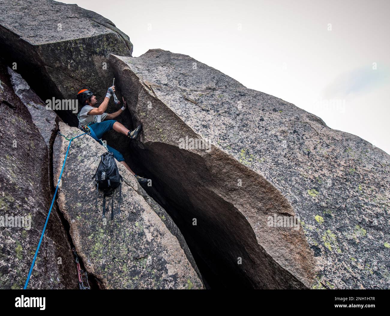 Ein Mann klettert auf eine Felswand, während er einen Rucksack schleppt Stockfoto