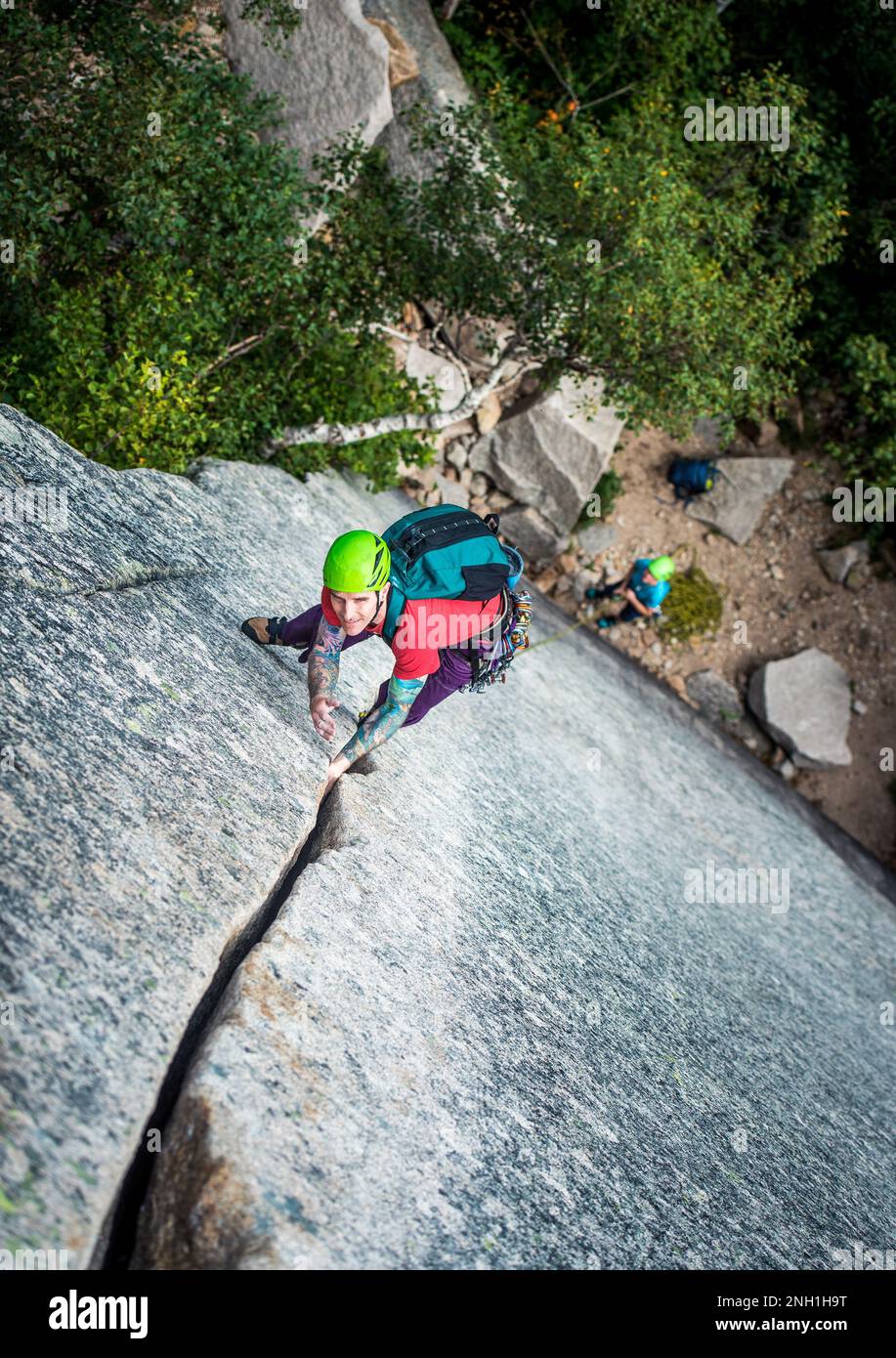 Ein Mann mit Tattoos klettert auf einen Riss an einer Felswand Stockfoto