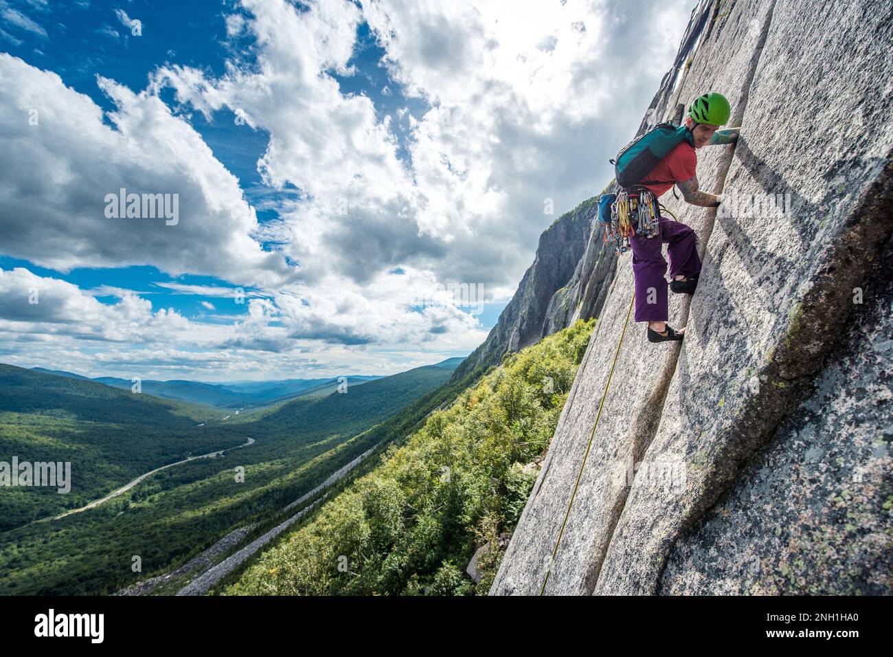 Ein Mann klettert steile Risse auf einer Klippe mit einem Tal dahinter Stockfoto