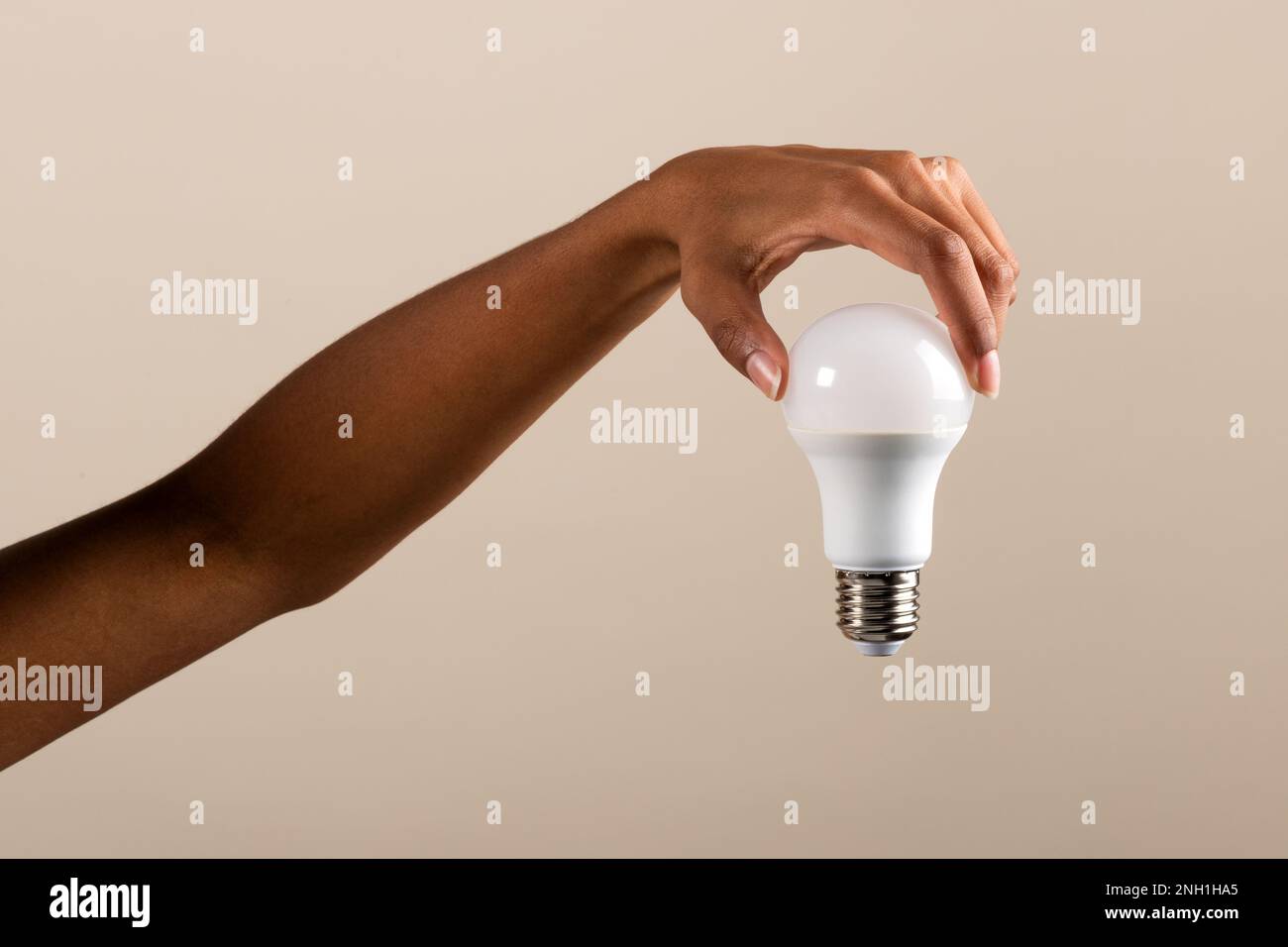 Anonyme afroamerikanische weibliche Hand mit moderner LED-Glühlampe vor beigefarbenem Hintergrund Stockfoto
