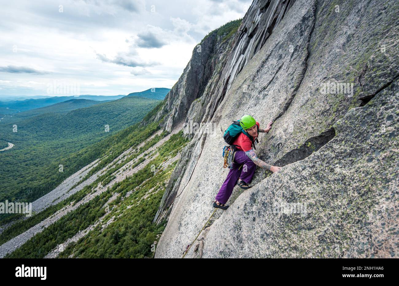 Ein Mann klettert steile Risse auf einer Klippe mit einem Tal dahinter Stockfoto