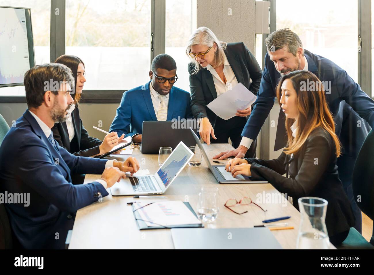 Gruppe multiethnischer Kollegen, die sich in formellen Kleidungsstücken am Tisch versammeln, während sie Laptops verwenden und Projektdetails besprechen, während sie an der Geschäftsstrategie in arbeiten Stockfoto