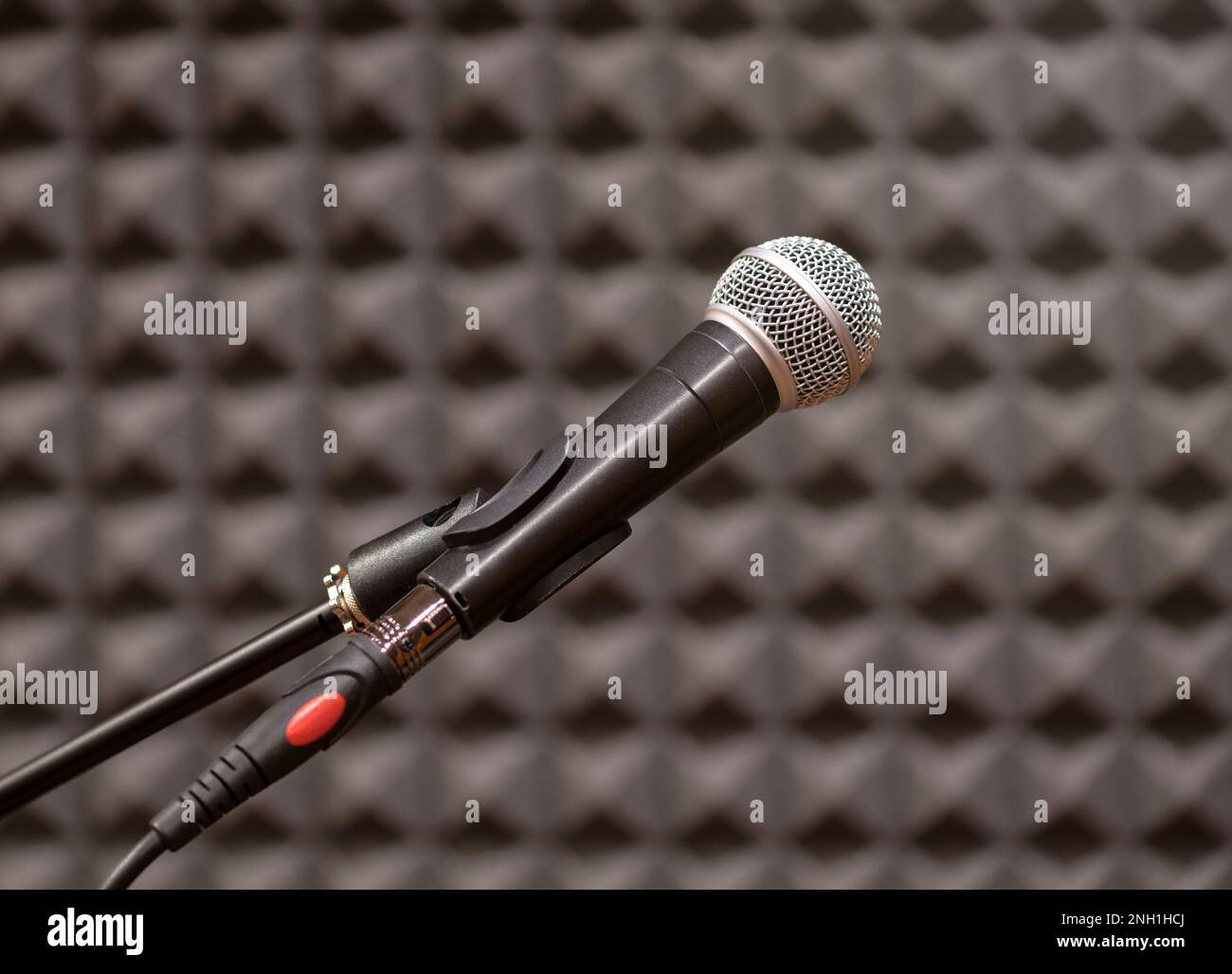 Modernes Mikrofon im Probenraum an verschwommener, schwarz strukturierter Wand mit selektivem Fokus platziert Stockfoto