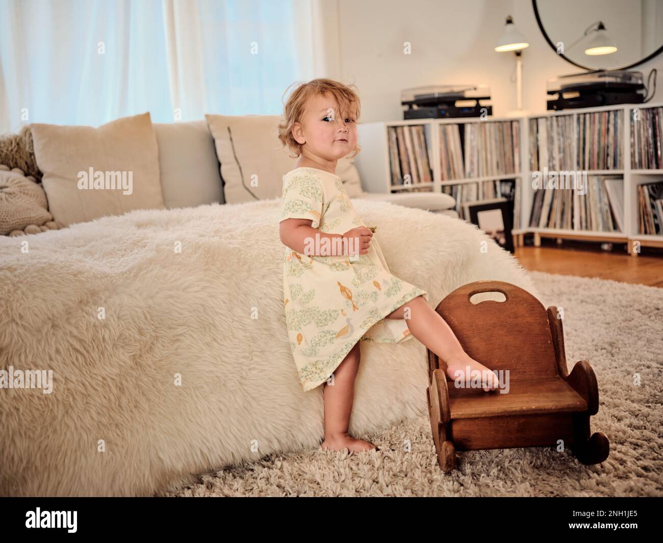 Kleinkind mit Bein auf einem hölzernen Schaukelstuhl im Wohnzimmer Stockfoto
