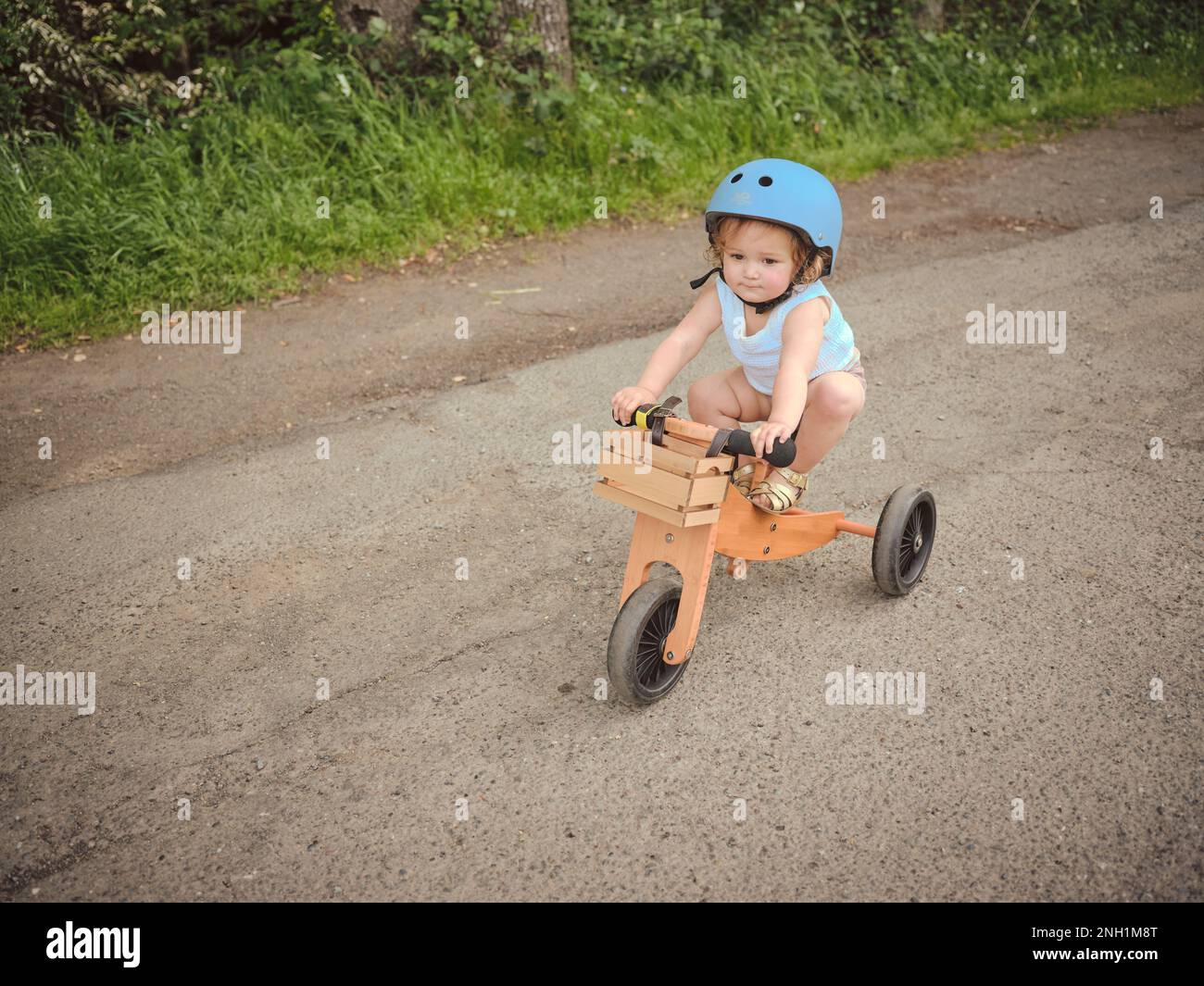 Ein Kleinkind mit blauem Tanktop fährt auf einem hölzernen Dreirad Stockfoto
