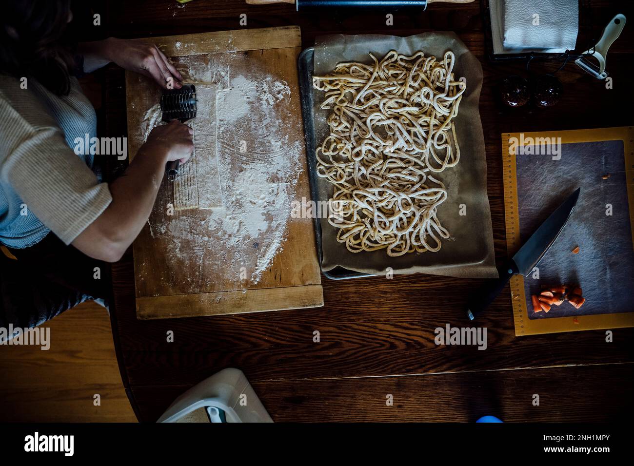 Blick von oben auf eine Frau, die hausgemachte Pasta auf dem Küchentisch schneidet Stockfoto