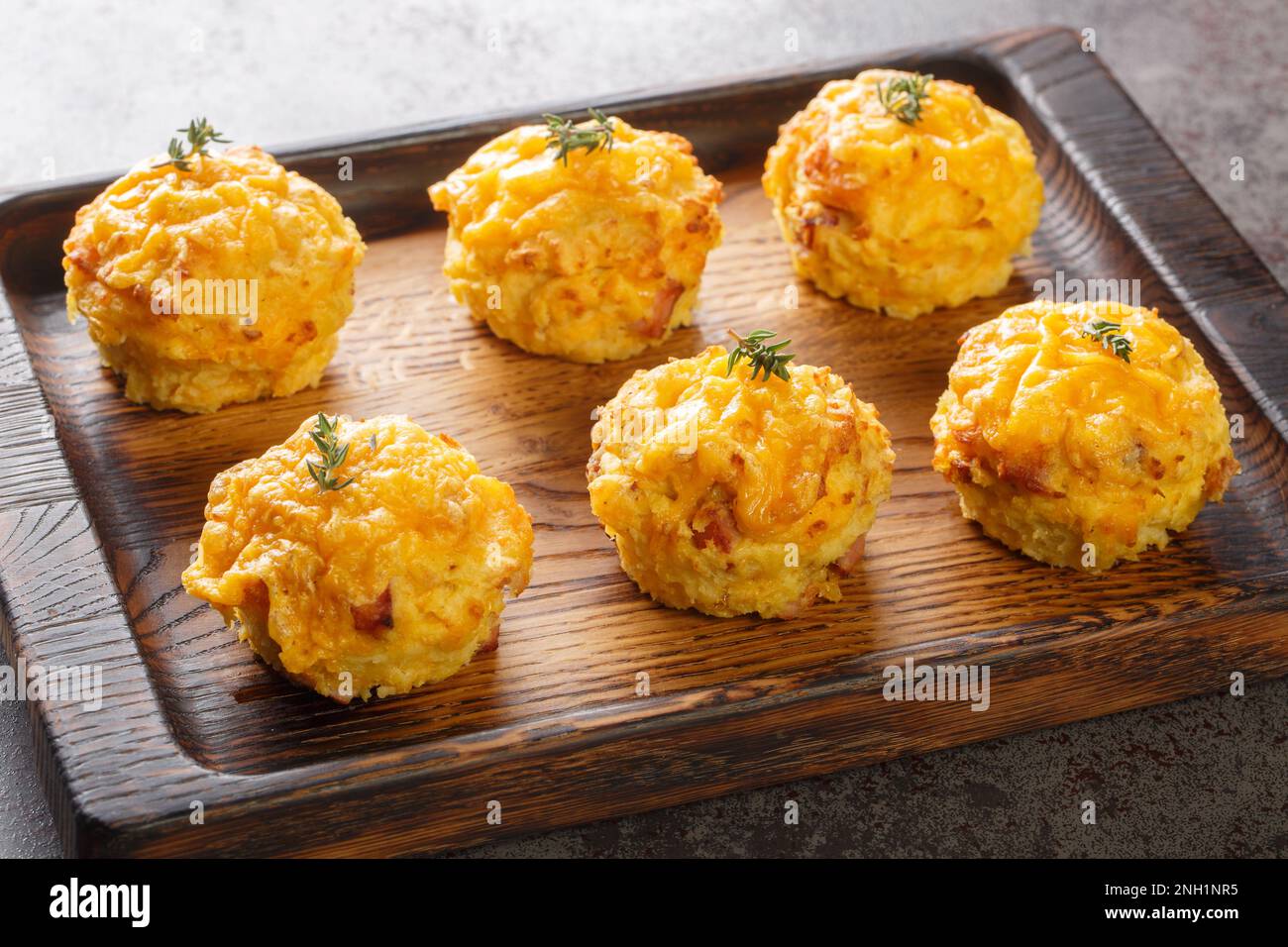 Zarte hausgemachte Muffins mit Kartoffeln, Zwiebeln, Speck und Cheddar aus der Nähe auf einem Holztablett auf dem Tisch. Horizontal Stockfoto
