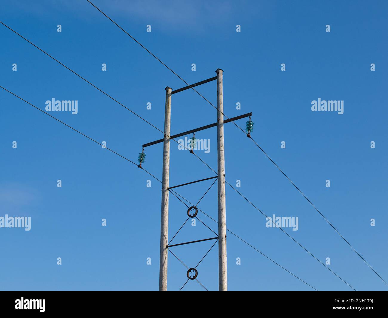 Drei Stromleitungen, die auf einem Querträger zwischen zwei Holzstangen aufgehängt sind. Leistungsisolatoren sind sichtbar. An einem sonnigen Tag mit blauem Himmel aufgenommen. Stockfoto