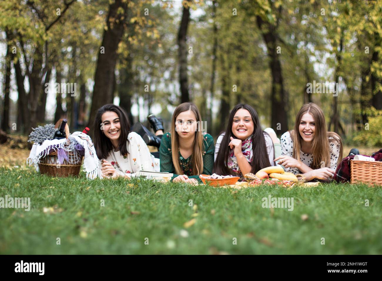 Eine Gruppe von vier Frauen, die ein lustiges Picknick im Park machen, auf einer Decke liegen, Essen und Natur genießen. Stockfoto