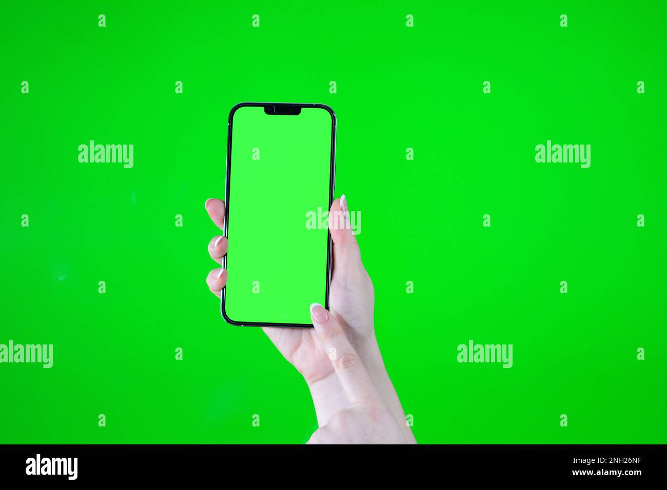 Bei weiblichen Händen zeigt ein grüner Bildschirm im Telefon auf grünem Hintergrund, während die andere Hand in die untere rechte Ecke zeigt Stockfoto