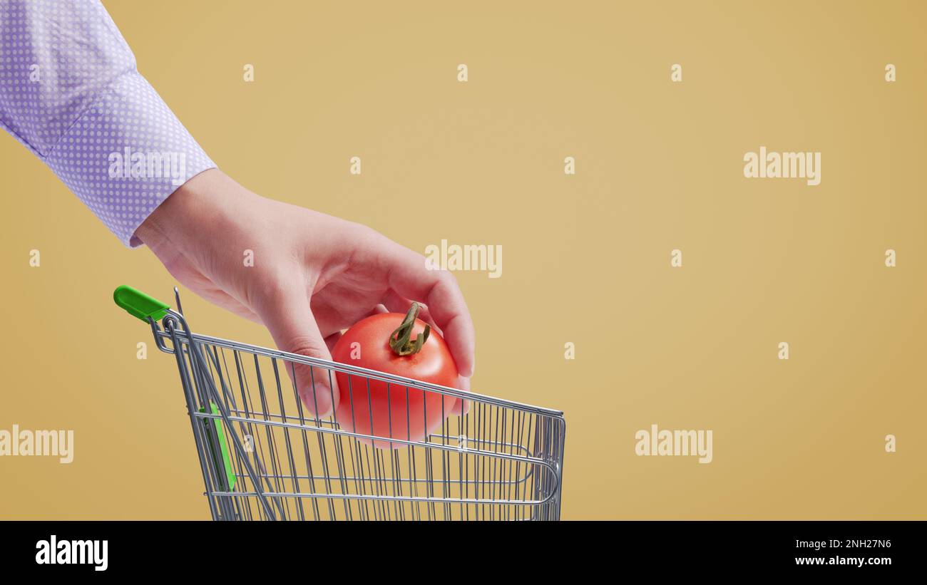 Kunde legt eine Tomate in einen kleinen Einkaufswagen, Lebensmitteleinkaufskonzept Stockfoto