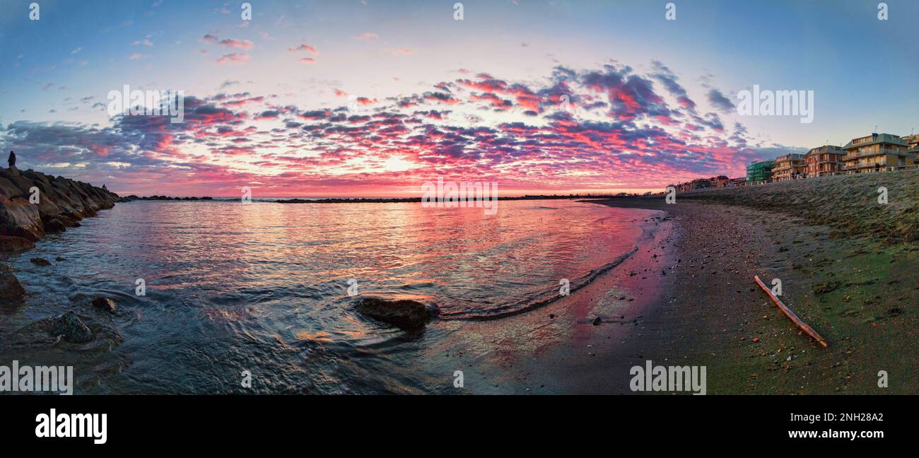 Die Sonne ging langsam zum Horizont hinab und warf ein warmes goldenes Licht über die ruhigen Gewässer des Strandes in Rom, Italien. Der Himmel war mit Hu bemalt Stockfoto