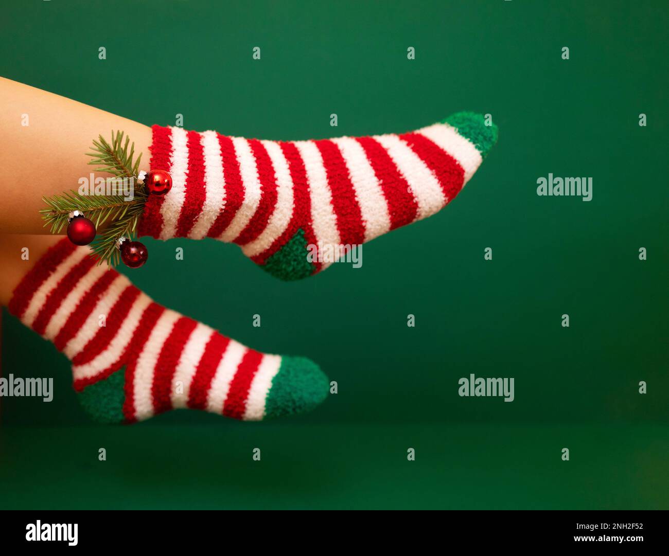 Gils Füße in flauschigen, warmen Socken für das neue Jahr. Weihnachtsbaum mit Kugeln schmückt das weibliche Bein. Die Farben der Socken sind rot-weiße Streifen und g Stockfoto