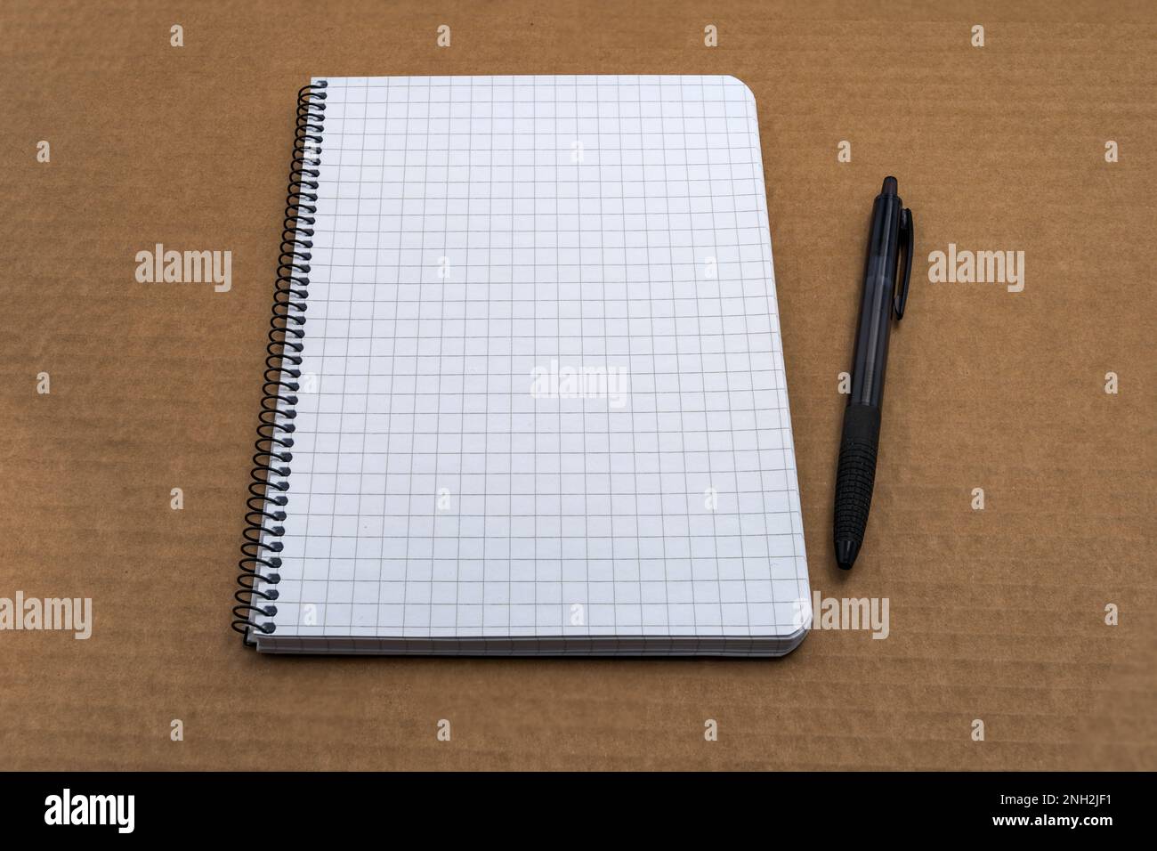 Kariertes Notizbuch mit Papierspirale und schwarzem Kugelschreiber auf braunem Karton Stockfoto