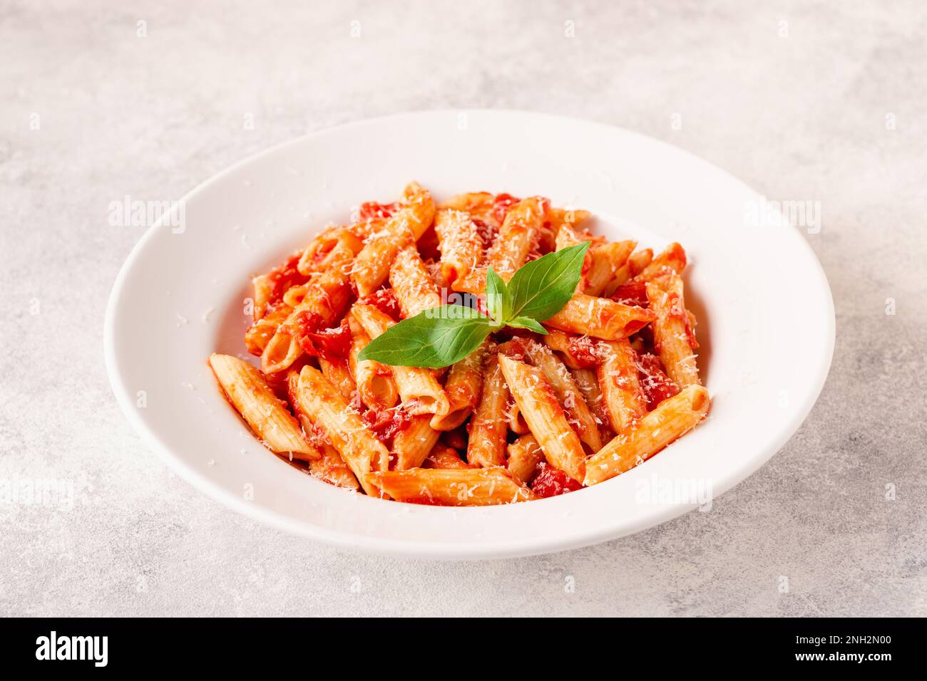 Klassische italienische Pasta Penne alla arrabiata mit frischem Basilikum auf hellem Hintergrund, selektiver Fokus Stockfoto