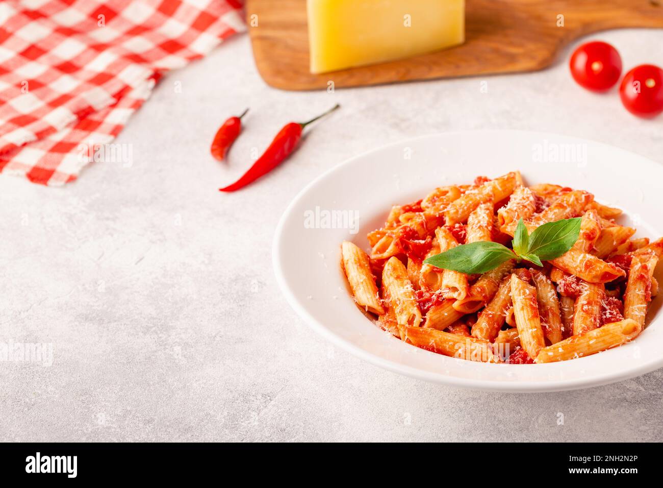 Klassische italienische Pasta Penne alla arrabiata mit frischem Basilikum auf hellem Hintergrund, selektiver Fokus Stockfoto