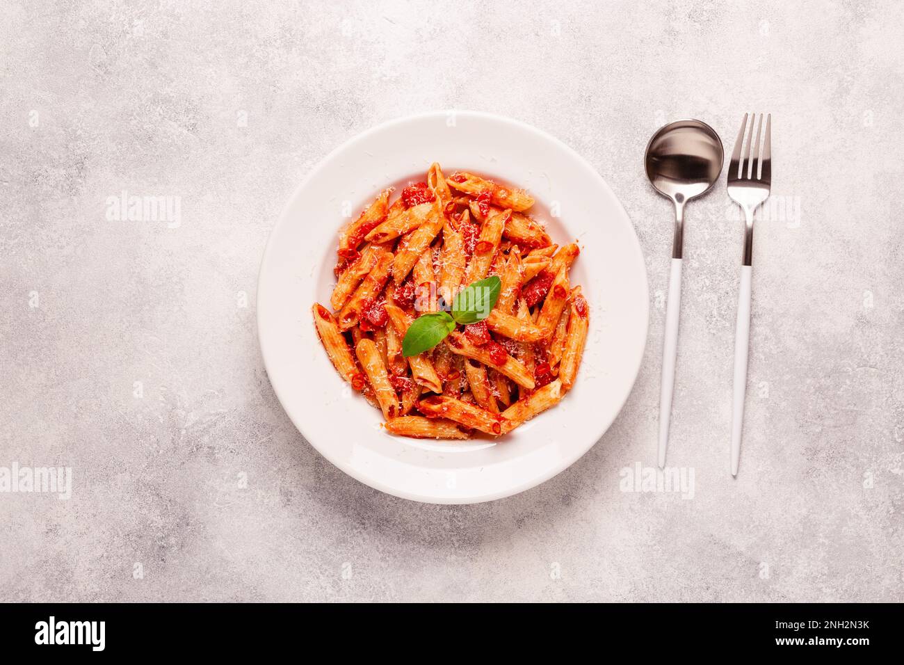 Klassische italienische Pasta Penne alla arrabiata mit frischem Basilikum auf hellem Hintergrund, Draufsicht Stockfoto