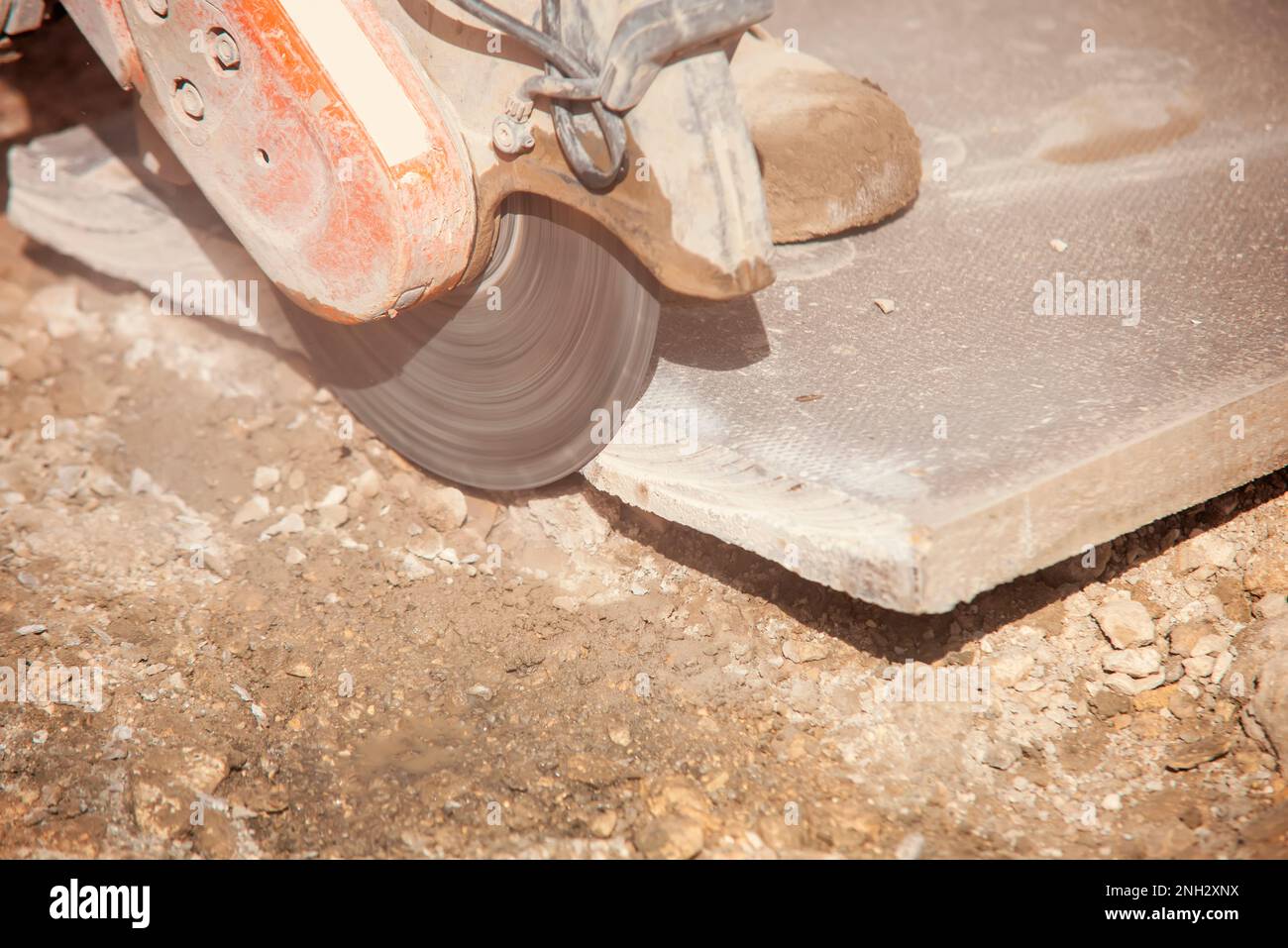 Baumeister schneidet Betonplatten mit einer Betonsäge und einer Diamantklinge während der Straßenpflasterarbeiten im Außenbereich Stockfoto
