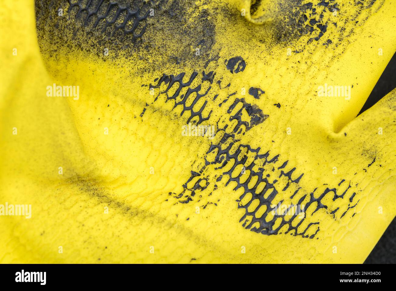 Schwarze Farbe auf die Oberfläche eines gelben Gummihandschuhs auftragen. Für eine schmutzige Metapher, oder für ein Chaos. Stockfoto