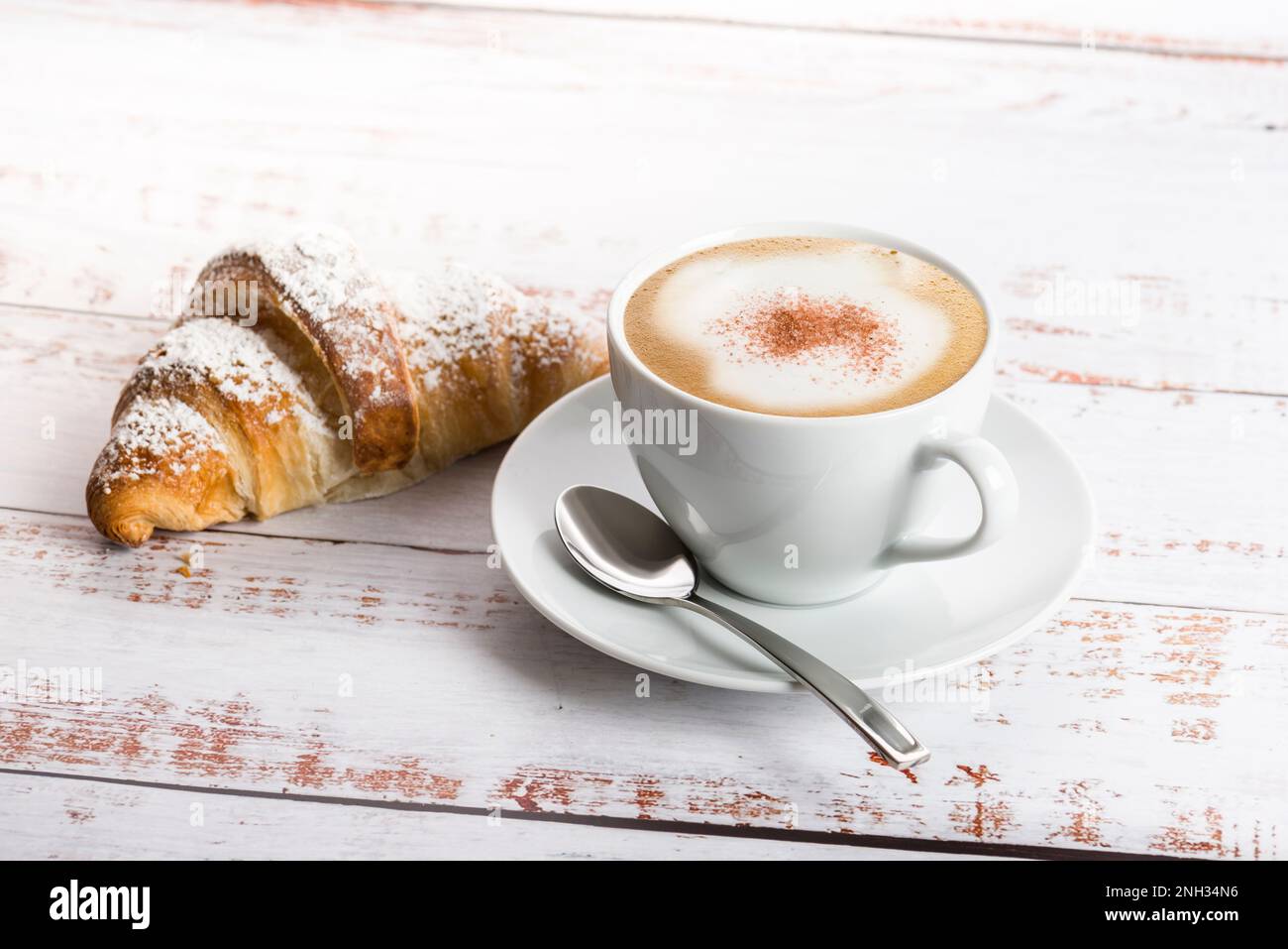 Frühstück mit Cappuccino und Croissant auf einem Holztisch. Stockfoto