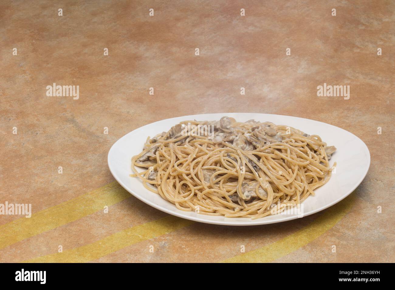 Rustikale Küchenablage mit bemalten Linien, die zu einer großen Platte mit saftigen Spaghetti mit Pilzen auf einem Teller führen, mit Kopierbereich. Stockfoto