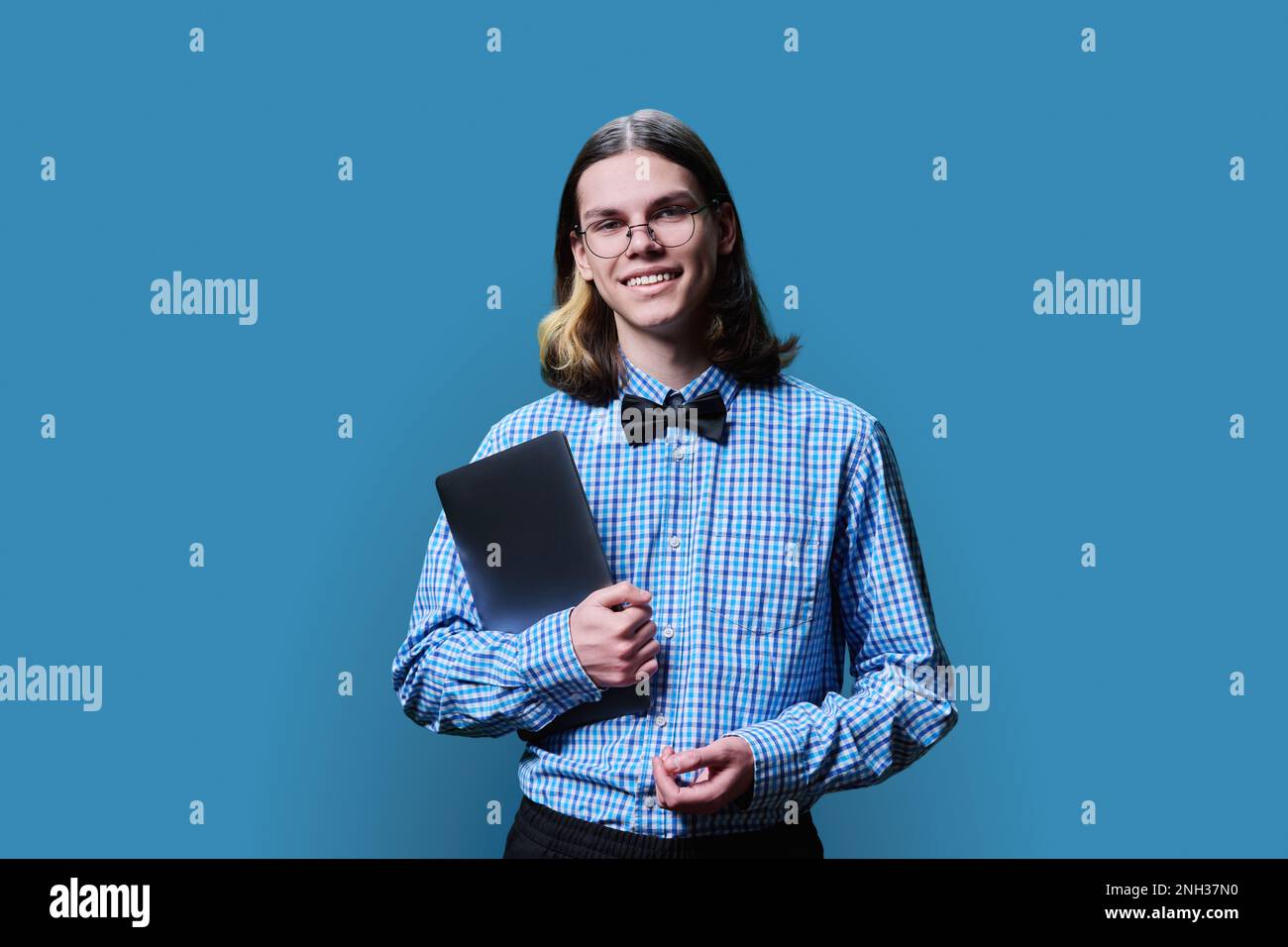 Ein schlauer Student mit Laptop, der in die Kamera schaut, blauer Hintergrund Stockfoto