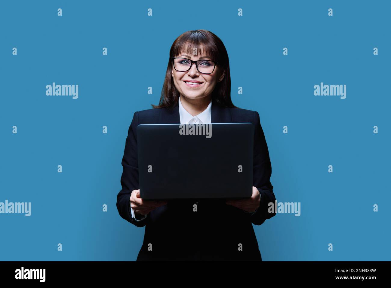 Reife Geschäftsfrau, die mit einem Notebook auf blauem Studiohintergrund posiert Stockfoto
