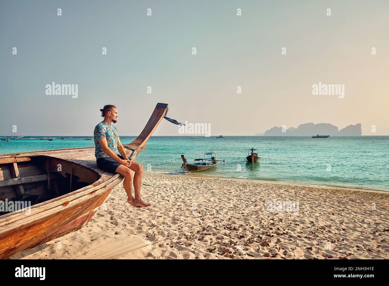 Mann sitzt auf dem Langboot am tropischen Sandstrand der Phi Phi Insel im Süden Thailands. Reisewanderlust-Magazin-Konzept. Stockfoto